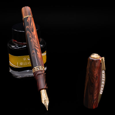 Visconti Medici Briarwood Fountain Pen in Gold uncapped, leaning on a bottle, showcasing the detailed gold nib.