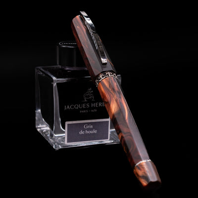 Visconti Medici Briarwood Fountain Pen in Ruthenium capped, leaning against an ink bottle. 