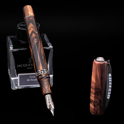 Visconti Medici Briarwood Fountain Pen in Ruthenium leaning on an ink bottle uncapped showcasing the detailing on the 18k nib.