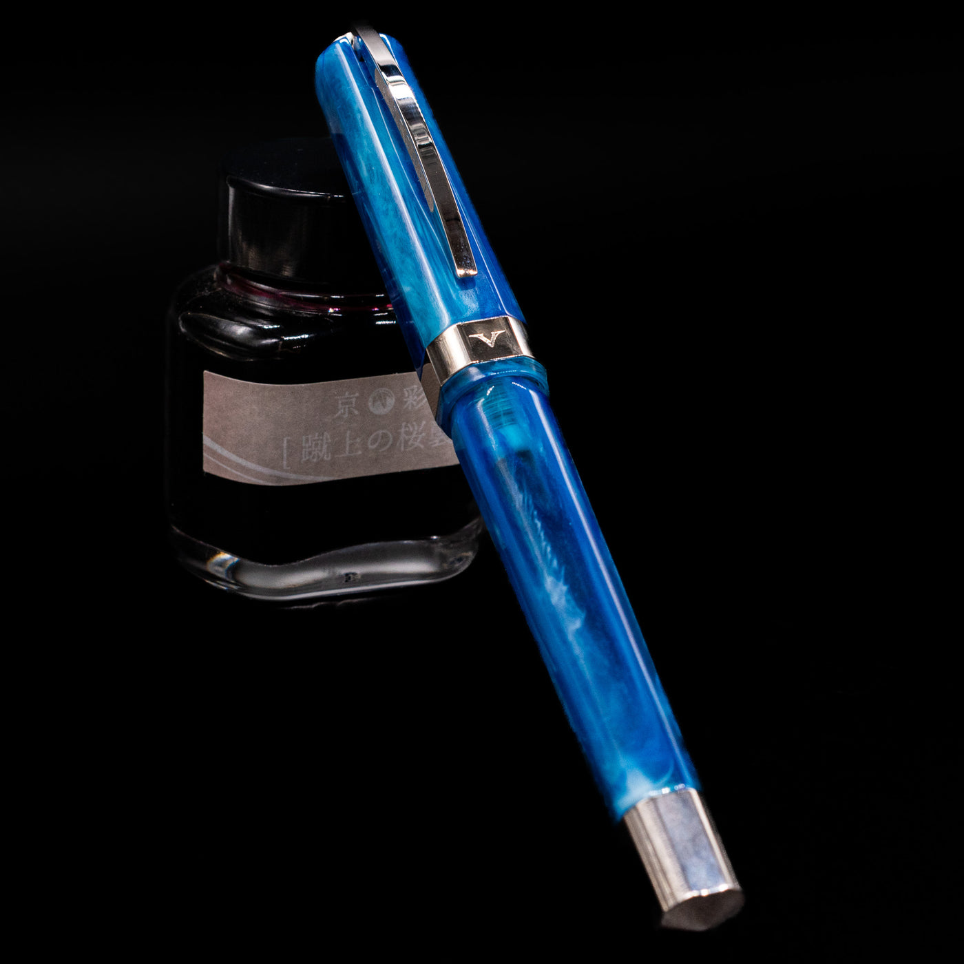 Visconti Opera Carousel Fountain Pen - Blue Cotton Candy capped, leaning against an ink bottle. 