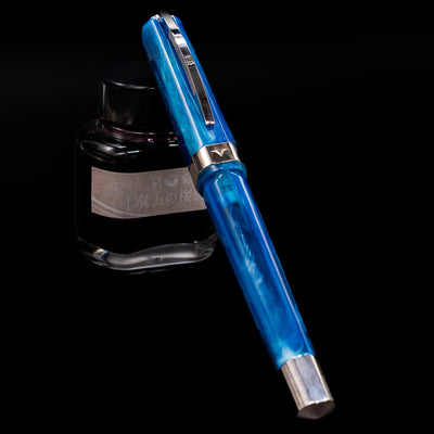 Visconti Opera Carousel Fountain Pen - Blue Cotton Candy capped, leaning against an ink bottle. 