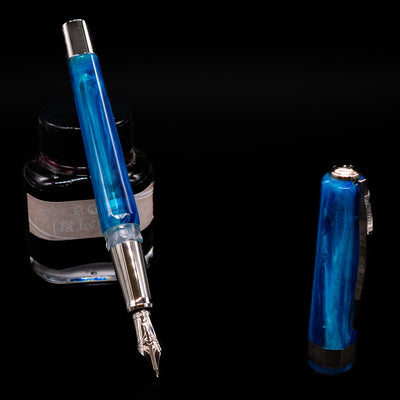 Visconti Opera Carousel Fountain Pen - Blue Cotton Candy leaning on an ink bottle uncapped showcasing the detailing on the nib.