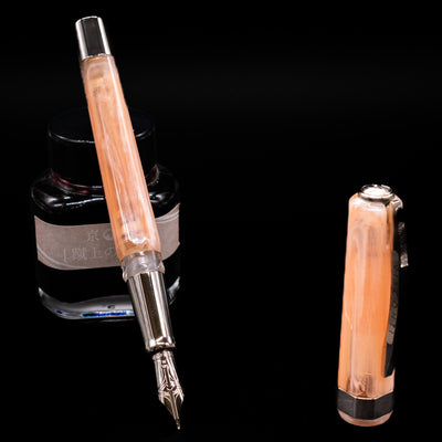 Visconti Opera Carousel Fountain Pen - Pink Blush leaning on an ink bottle uncapped showcasing the detailing on the nib.