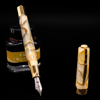 Visconti Opera Club Honey Almond Resin Fountain Pen - Preowned leaning on an ink bottle uncapped showcasing the detailing on the nib.