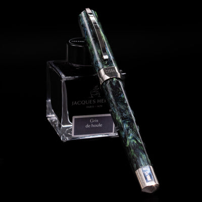 Visconti Opera Master Fountain Pen - Stargazer capped, leaning against an ink bottle. 