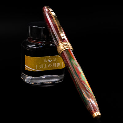 Visconti Van Gogh Fountain Pen - Flowering Plum Orchard capped, leaning against an ink bottle. 
