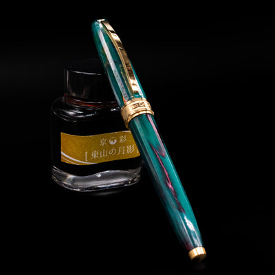 Visconti Van Gogh Fountain Pen - The Novel Reader capped, leaning against an ink bottle. 