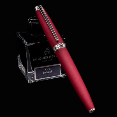 Caran d’Ache Léman V2 Burgundy fountain pen, capped and resting on an ink bottle