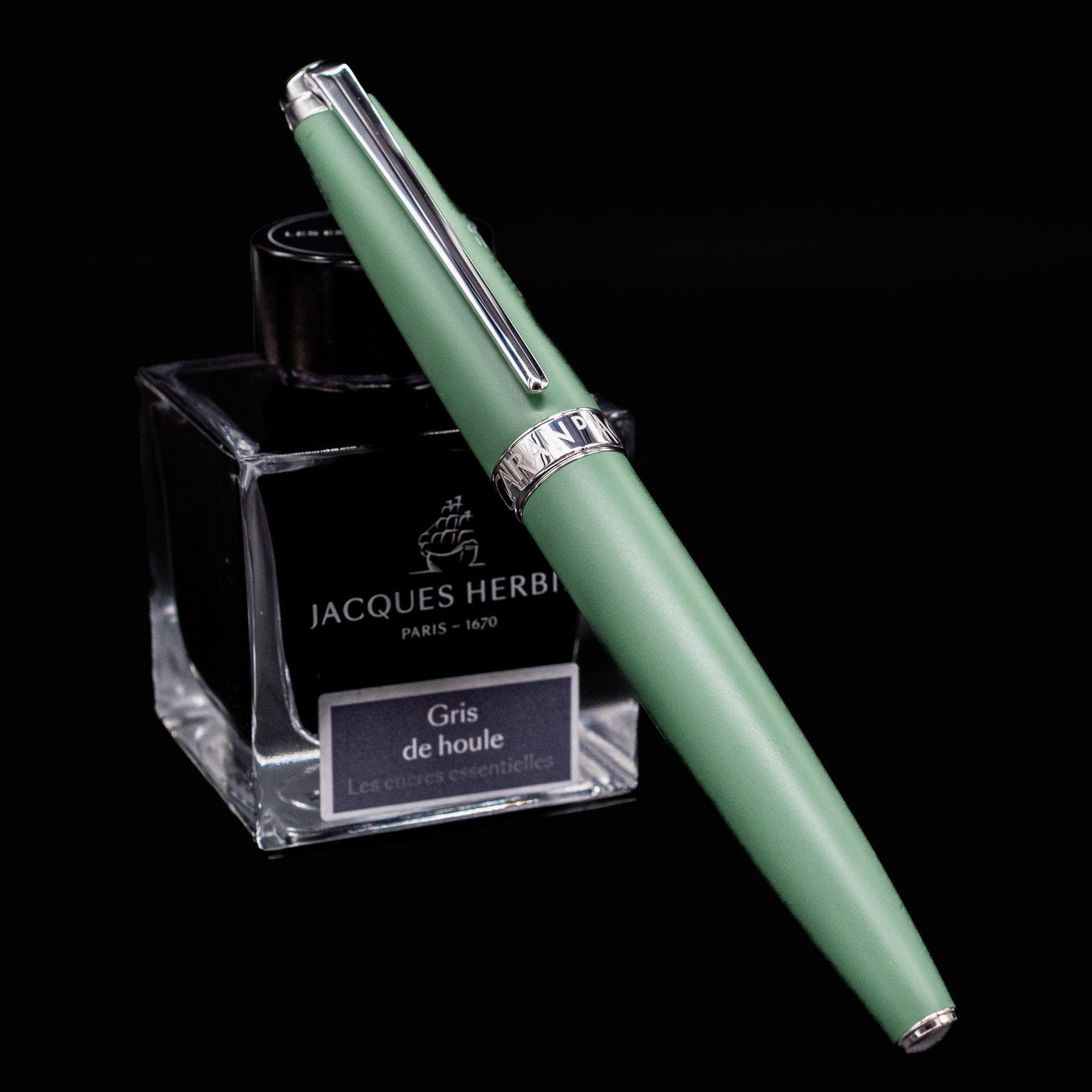 Caran d’Ache Léman V2 Vert de Gris fountain pen, capped and resting elegantly against a bottle of ink.

