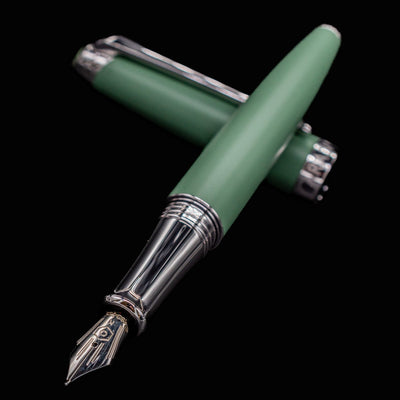Uncapped Caran d’Ache Léman Vert de Gris pen with body resting on cap, 18k gold nib aimed toward the camera.

