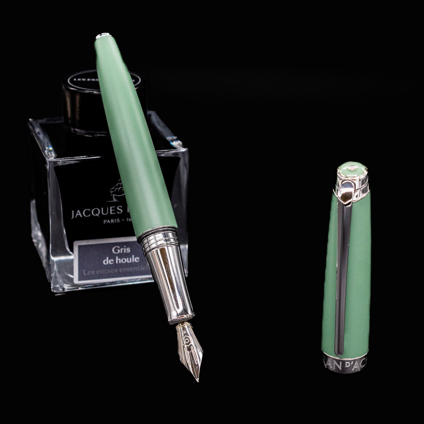 Caran d’Ache Léman Vert de Gris fountain pen, uncapped and leaning against an ink bottle, showing satin lacquer and nib.

