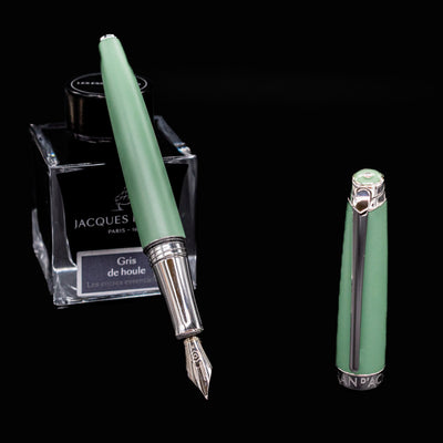 Caran d’Ache Léman Vert de Gris fountain pen, uncapped and leaning against an ink bottle, showing satin lacquer and nib.

