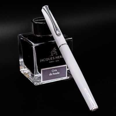 Diplomat Traveller Fountain Pen in White with Chrome Trim resting on Jacques Herbin Gris de Houle ink bottle
