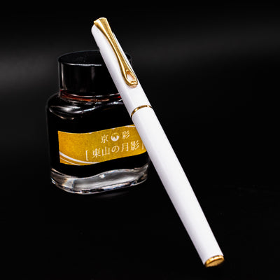 Diplomat Traveller White & Gold Fountain Pen shown capped in front of an ink bottle