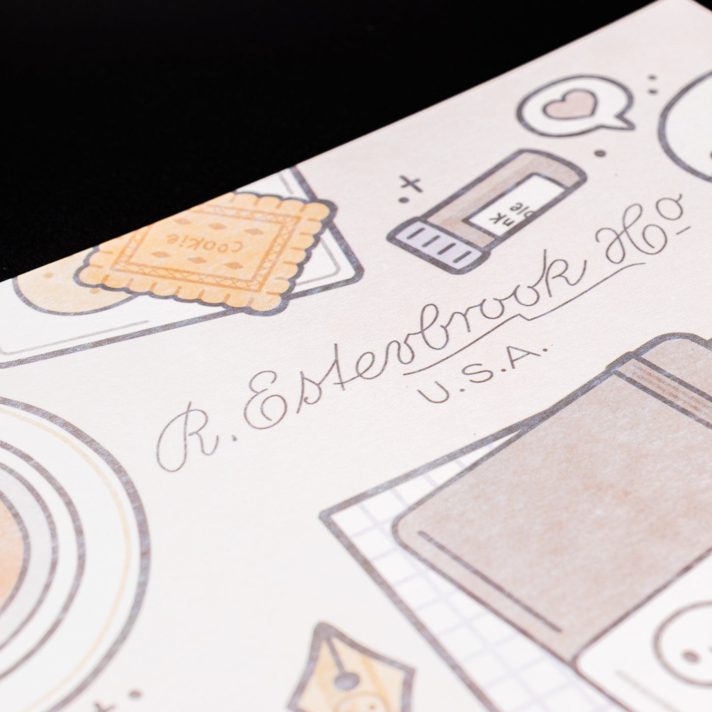 Close-up of Esterbrook x TheCoffeeMonsterzCo blotter paper showing detailed cookie and stationery illustrations in soft brown tones.