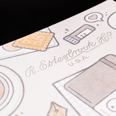 Close-up of Esterbrook x TheCoffeeMonsterzCo blotter paper showing detailed cookie and stationery illustrations in soft brown tones.