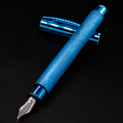 Faber-Castell Ambition Fountain Pen - Blue Wood uncapped at an angle, showing polished nib and cap in background.