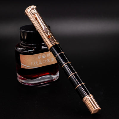 Graf von Faber-Castell Classic Anello Rose Gold fountain pen shown capped at a diagonal angle beside a red ink bottle.