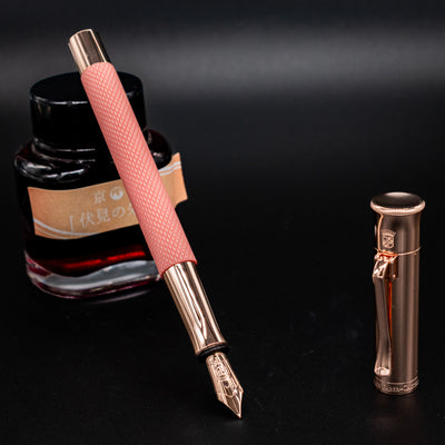 Close-up of Graf von Faber-Castell Guilloche Fountain Pen - Rose with cap off and nib angled near ink bottle