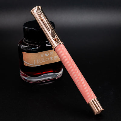 Graf von Faber-Castell Guilloche Fountain Pen - Rose capped and resting against ink bottle