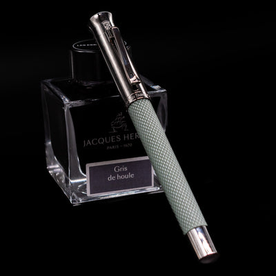 Graf von Faber-Castell Guilloche Fountain Pen in Sage Green, capped and resting on Jacques Herbin ink bottle