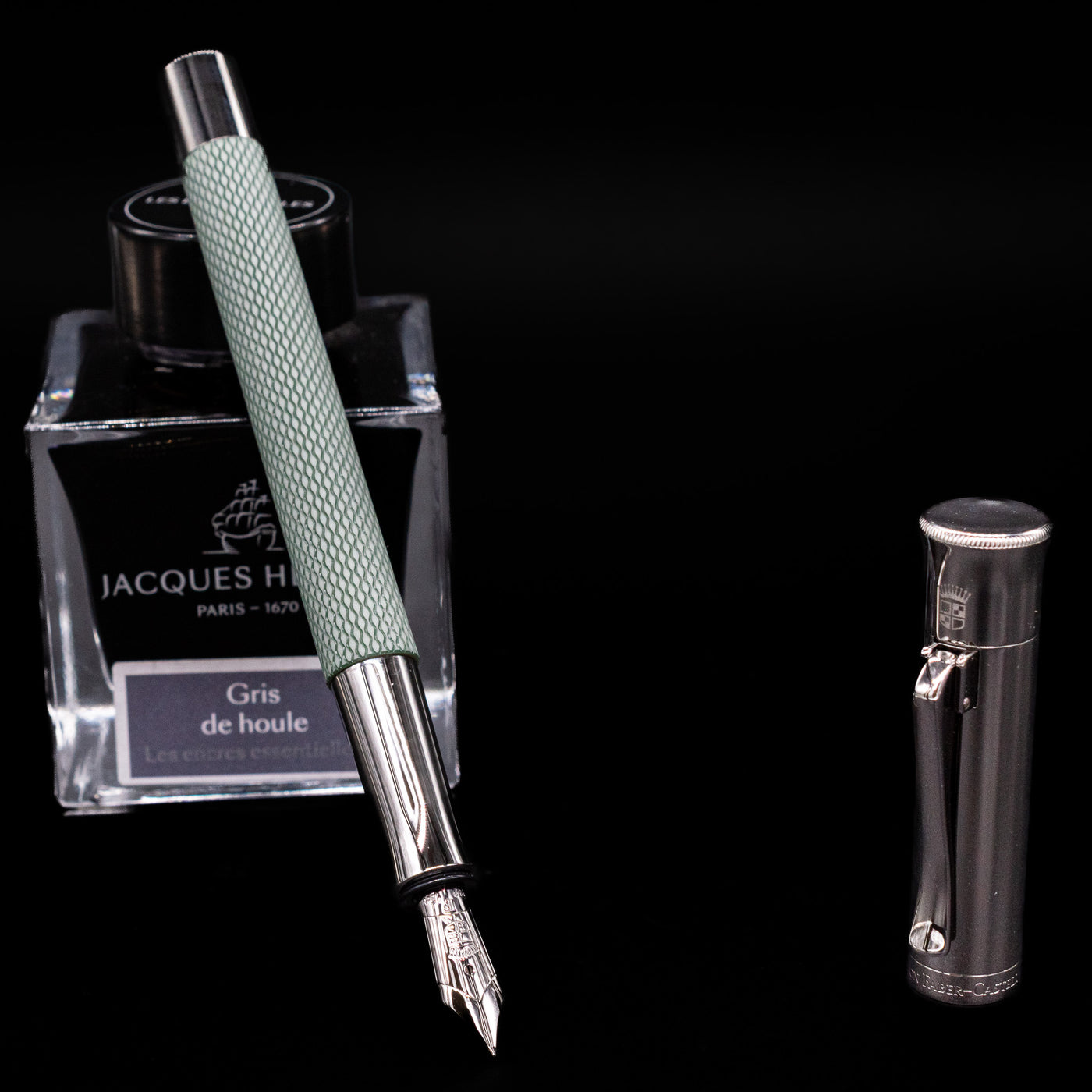 Graf von Faber-Castell Guilloche Fountain Pen in Sage Green with nib exposed, leaning on Jacques Herbin Gris de Houle ink bottle