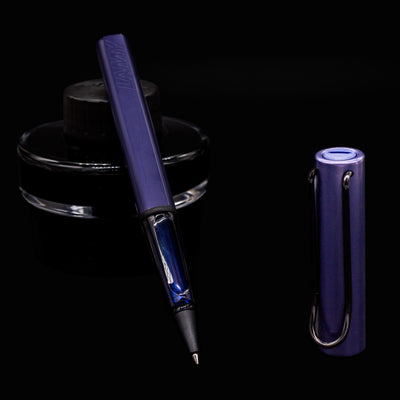 LAMY Al-Star Rollerball Pen in Dark Dusk uncapped with ink bottle background, showing transparent grip section