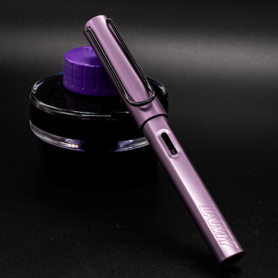 LAMY Al-Star Special Edition Fountain Pen in Aubergine shown capped and leaning on a purple ink bottle.