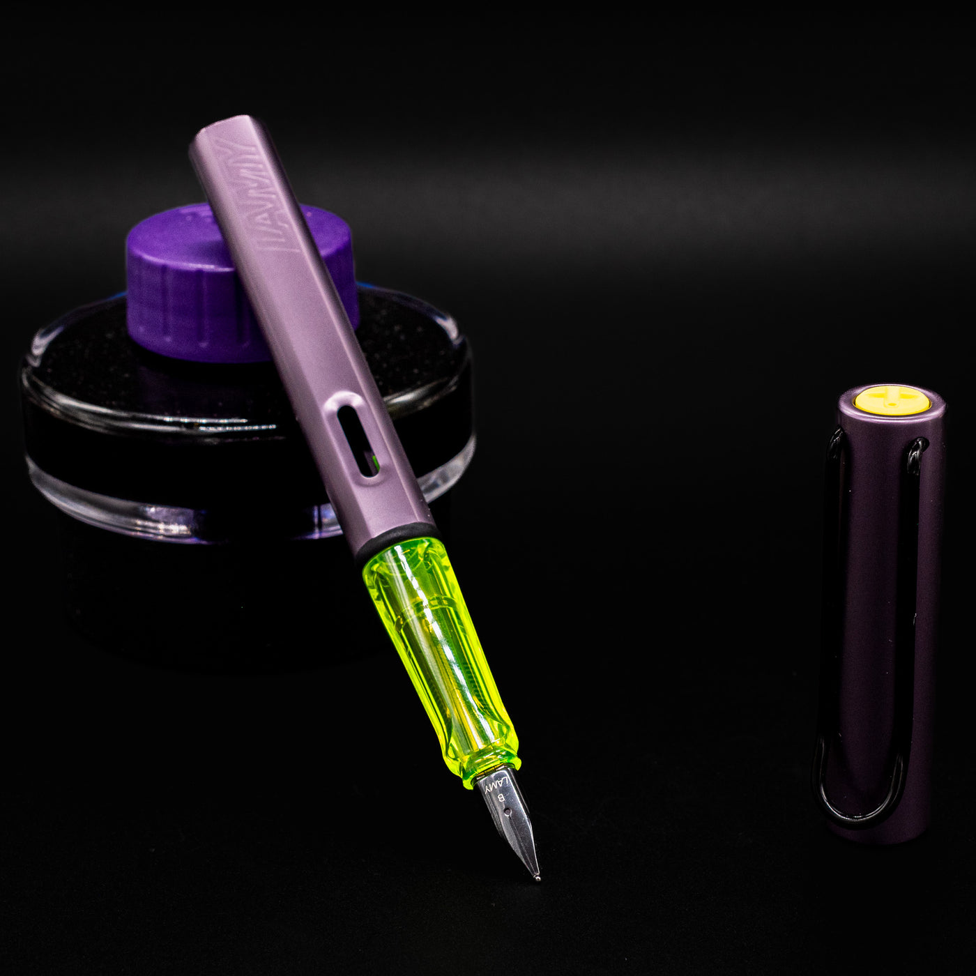 Uncapped LAMY Al-Star Special Edition Aubergine Fountain Pen next to a purple ink bottle, revealing neon yellow grip and steel nib.