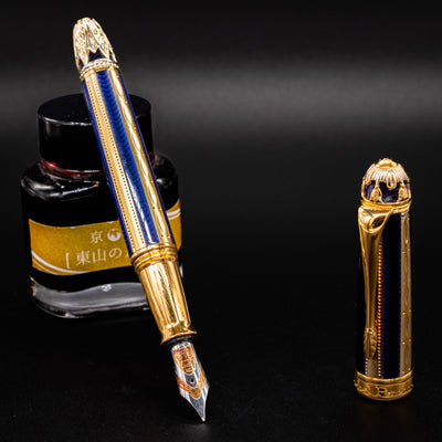 Uncapped Michel Perchin Fabergé fountain pen beside ink bottle, revealing ornate nib and pen body.