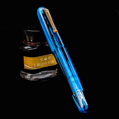 Molteni Modelo 71 Fountain Pen in Blue & Gold shown capped beside an ink bottle on black background.