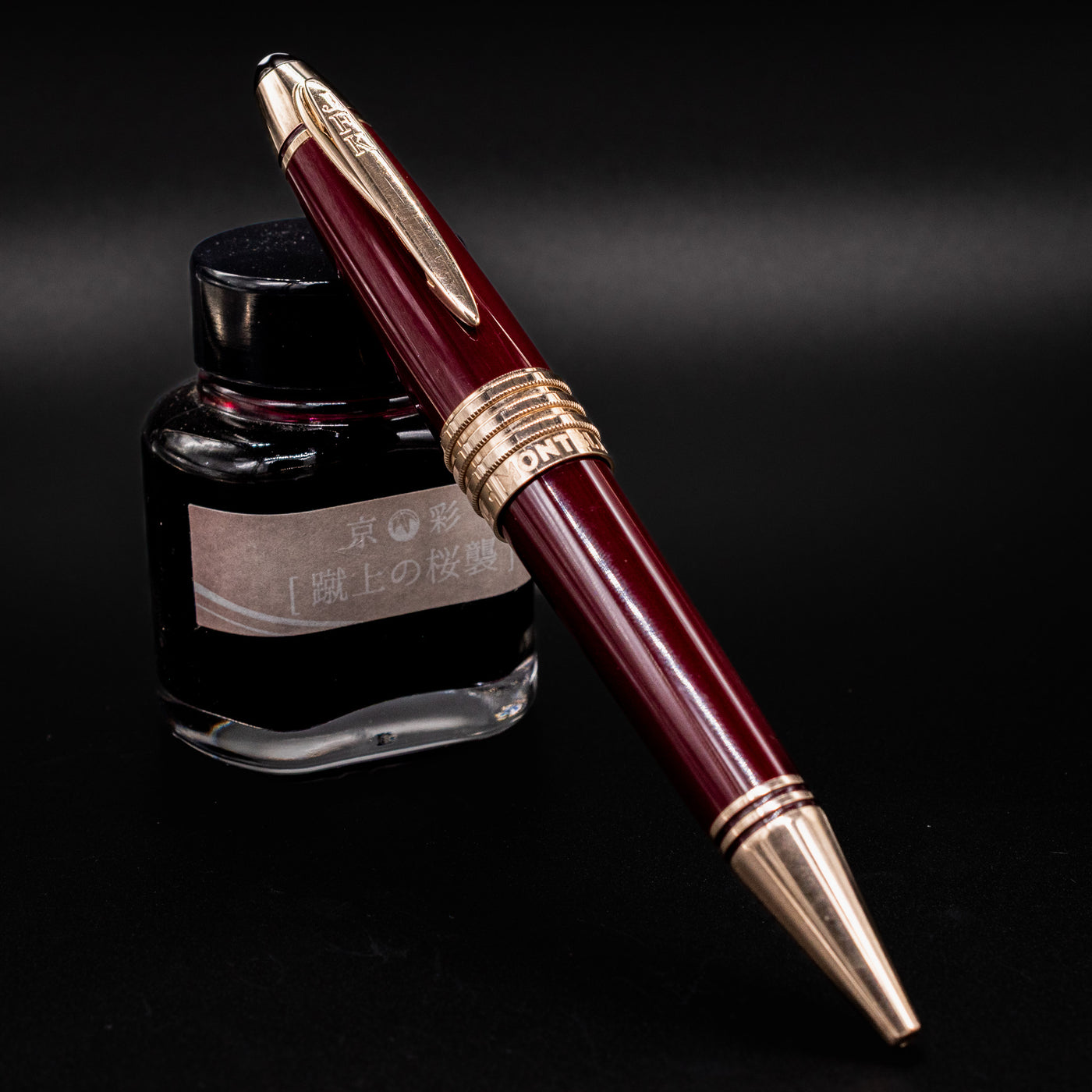 Preowned Montblanc Great Characters John F. Kennedy Burgundy Ballpoint Pen displayed with ink bottle for visual contrast.