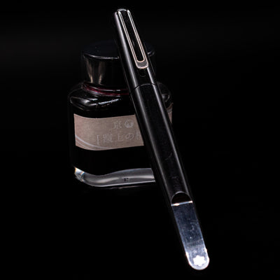 capped montblanc marc newson black resin rollerball pen leaning on an ink bottle