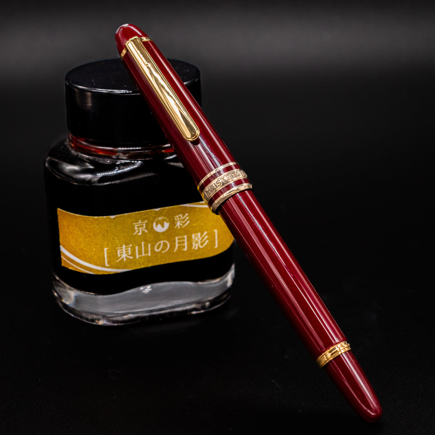 Montblanc Meisterstuck 114R Bordeaux & Gold Mozart Fountain Pen shown capped and resting against a yellow-labeled ink bottle – Preowned