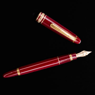 Flatlay of the Montblanc Meisterstuck 114R Bordeaux & Gold Mozart Fountain Pen – Preowned, uncapped with the nib and cap displayed separately.