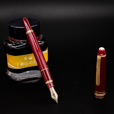 Montblanc Meisterstück 114R Bordeaux Mozart fountain pen shown uncapped with gold nib and ink bottle