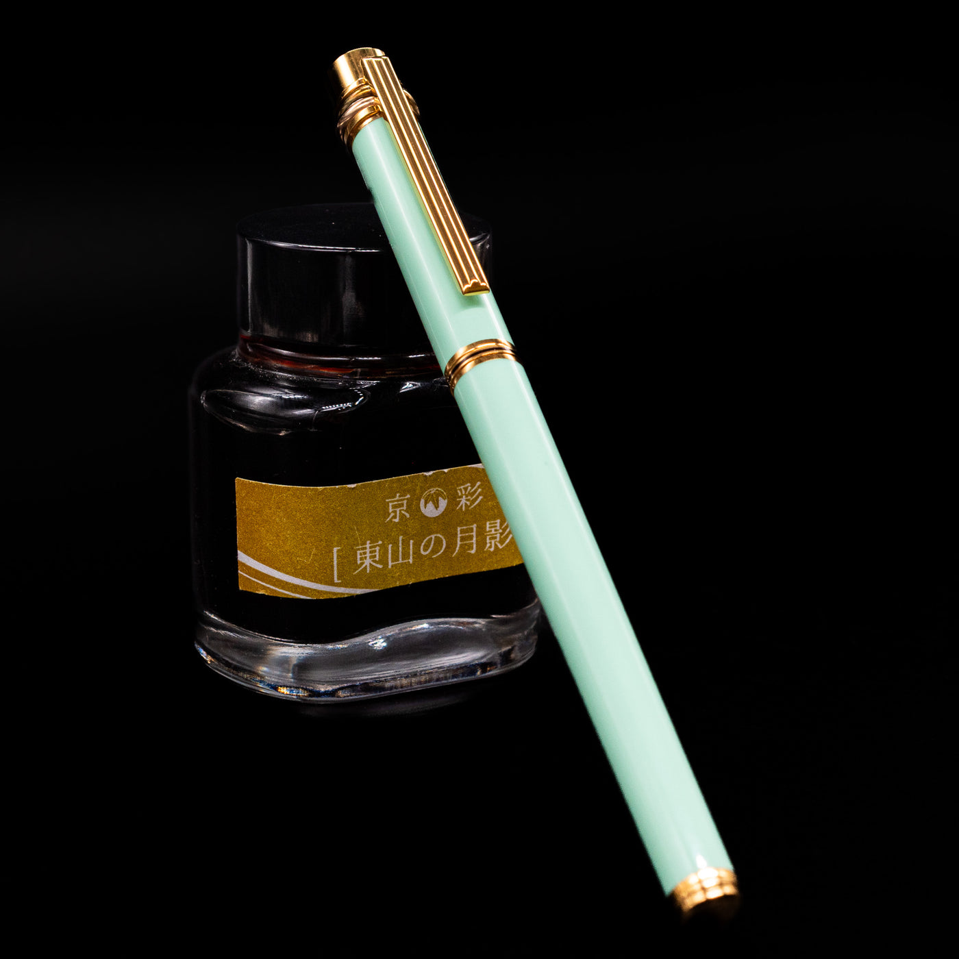 Capped Must de Cartier Trinity Tiffany Blue Fountain Pen leaning against yellow-labeled ink bottle