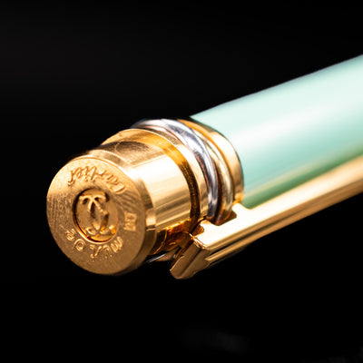 Detailed macro of Must de Cartier Trinity Fountain Pen cap finial with gold, rose gold, and platinum-tone rings and engraved logo