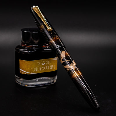 Namiki Yukari Double Crane capped fountain pen resting on ink bottle.