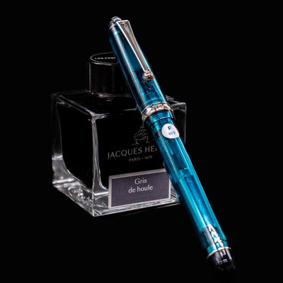 Full view of Pilot Custom 74 Teal Fountain Pen resting against Jacques Herbin ink bottle