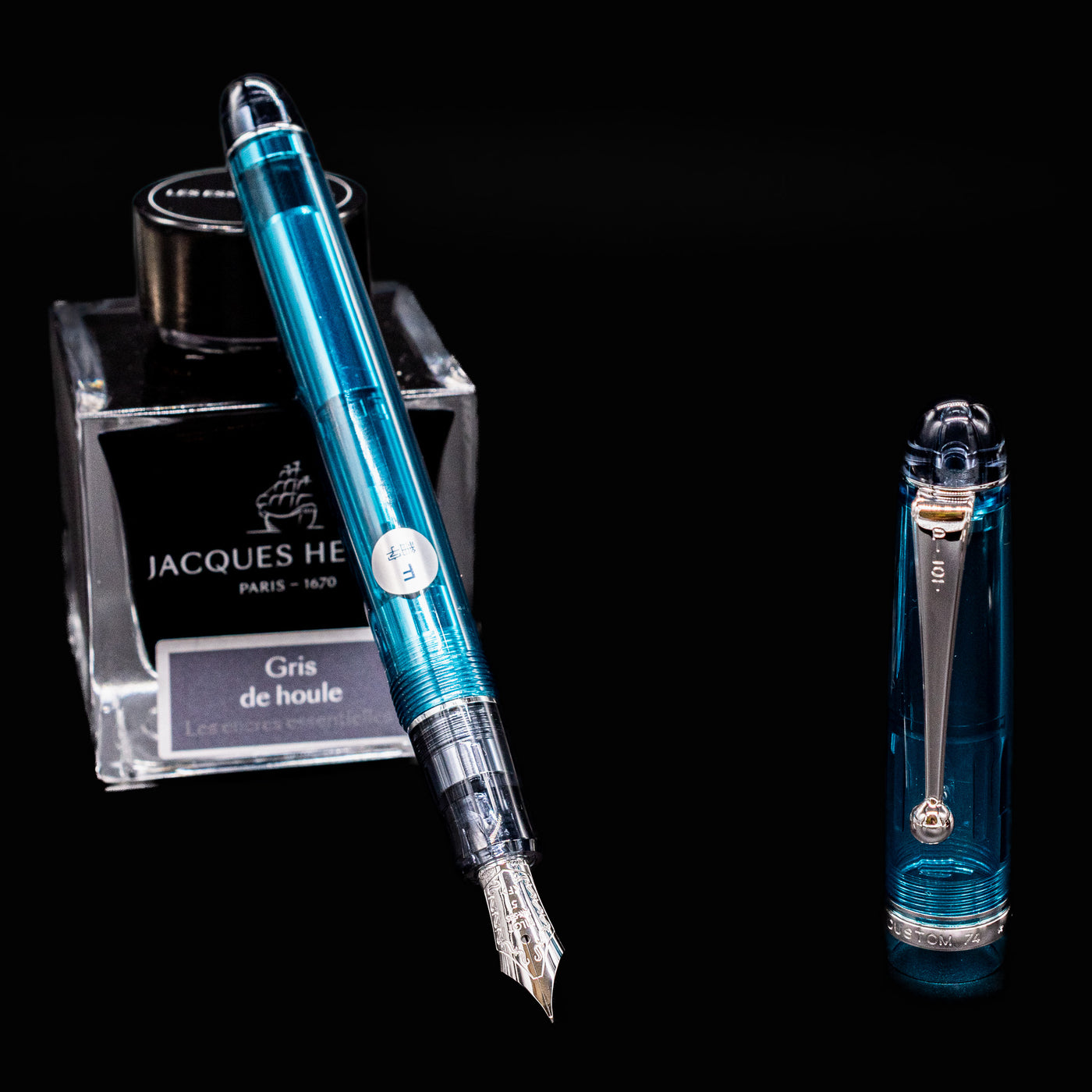 Pilot Custom 74 Teal Fountain Pen displayed with Jacques Herbin Gris de Houle ink bottle on black background