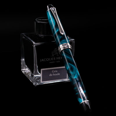 Pilot Custom Heritage SE Green Marble Fountain Pen shown capped, displayed diagonally across a Jacques Herbin Gris de Houle ink bottle