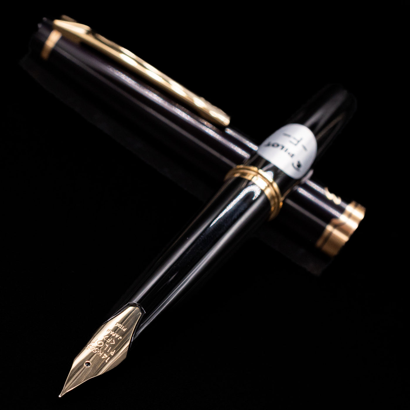 Angled view of Pilot E95S Fountain Pen in Black showing gold nib and capped pen in background