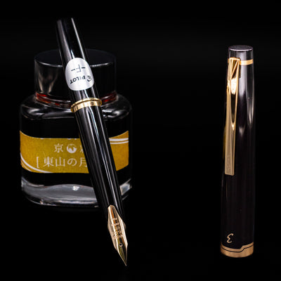 Pilot E95S Fountain Pen in Black open with gold nib, positioned in front of yellow-labeled ink bottle