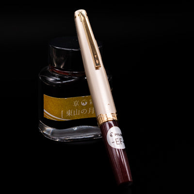 Pilot E95S Fountain Pen in Burgundy and Ivory with cap on, positioned against yellow label ink bottle