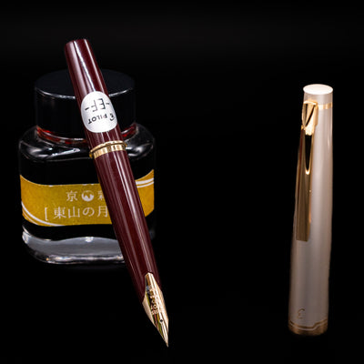 Pilot E95S Fountain Pen in Burgundy and Ivory with gold nib resting on yellow ink bottle