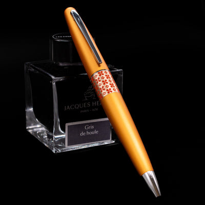 Pilot Metropolitan Pop Ballpoint Pen in Orange resting on a Jacques Herbin ink bottle, showcasing the pen’s modern design.