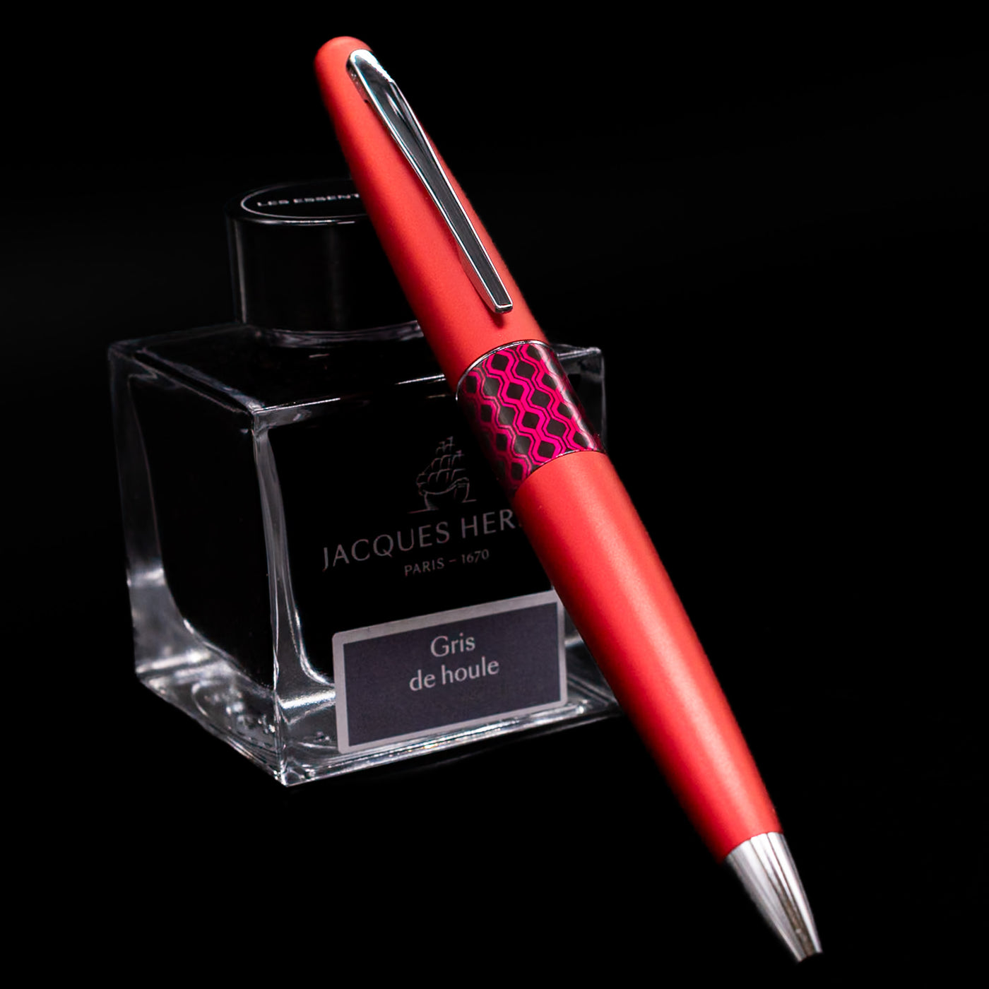 Pilot Metropolitan Pop Ballpoint Pen in red leaning against Jacques Herbin ink bottle, showcasing metallic body and pop art center band.