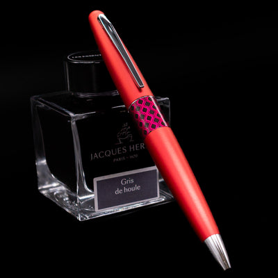 Pilot Metropolitan Pop Ballpoint Pen in red leaning against Jacques Herbin ink bottle, showcasing metallic body and pop art center band.
