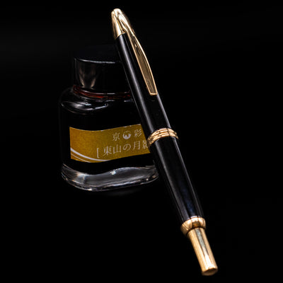 Capped Pilot Vanishing Point Fountain Pen in black and gold leaning on Kyo-no-oto ink bottle
